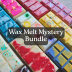 A close-up of multiple colorful wax melts arranged in rectangular bars, with a dark translucent banner across the center reading 'Wax Melt Mystery Bundle.' The wax melts come in pink, red, yellow, blue, white, and multicolor speckled designs.